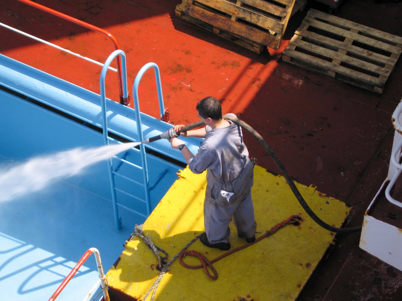 services-01 A worker using a high-pressure hose to clean the deck of a ship, showing industrial processes.