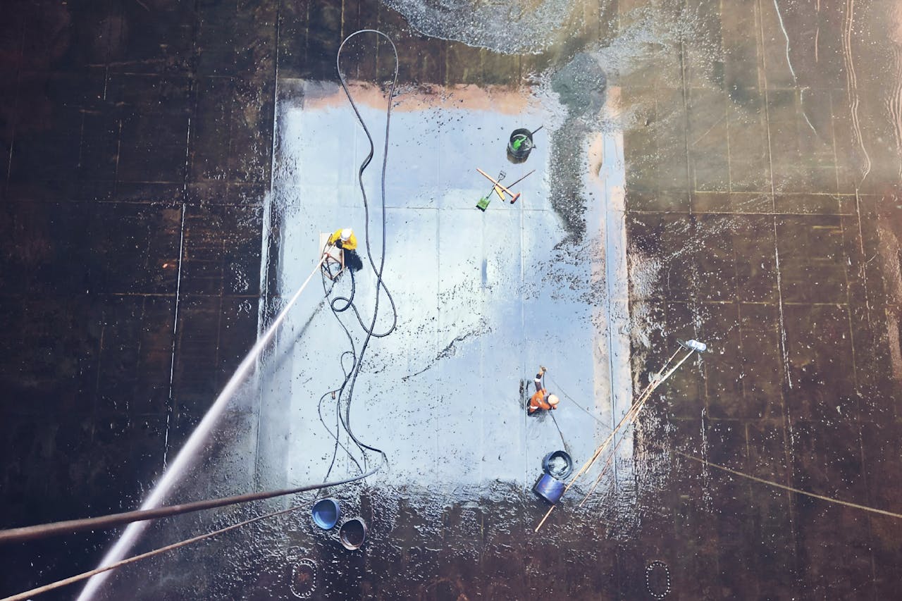 services-03 Top view of workers cleaning a large surface with equipment and water hoses.