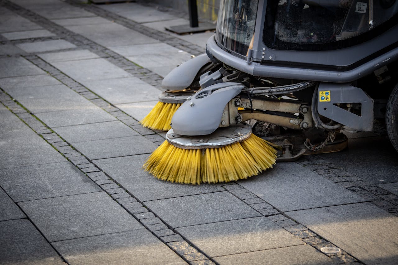 why-choose-us Close-up view of a road sweepers yellow brushes on a paved street.