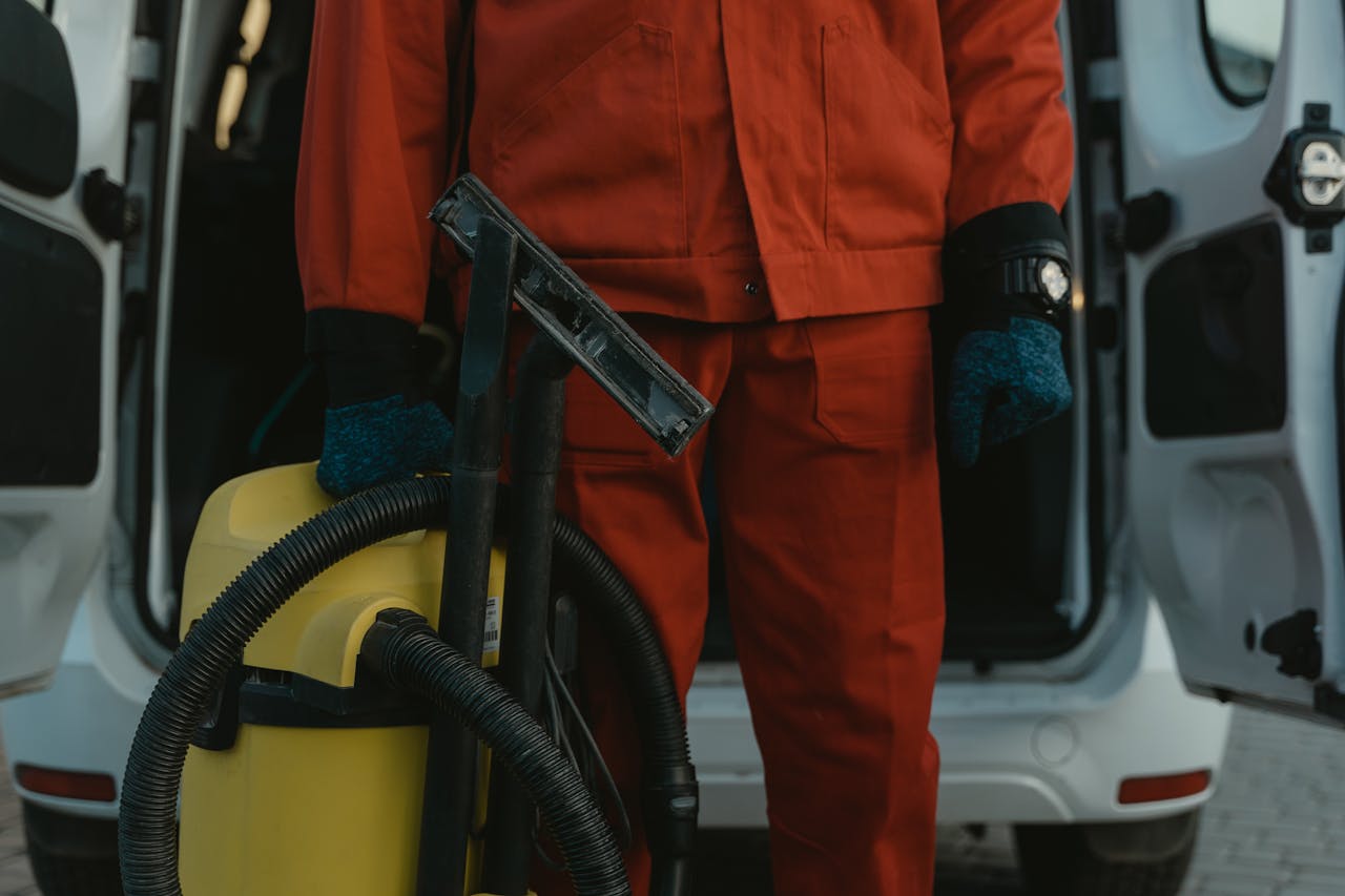 about-01 A professional cleaner in a red uniform holding a vacuum near a van, ready for service.